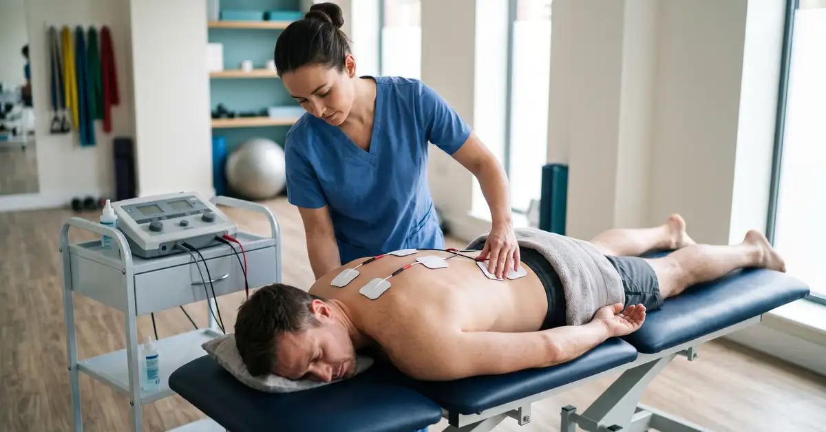 Chartered physiotherapist positioning interferential therapy electrodes on a patient's lower back at CK Physio, Hanwell, West London